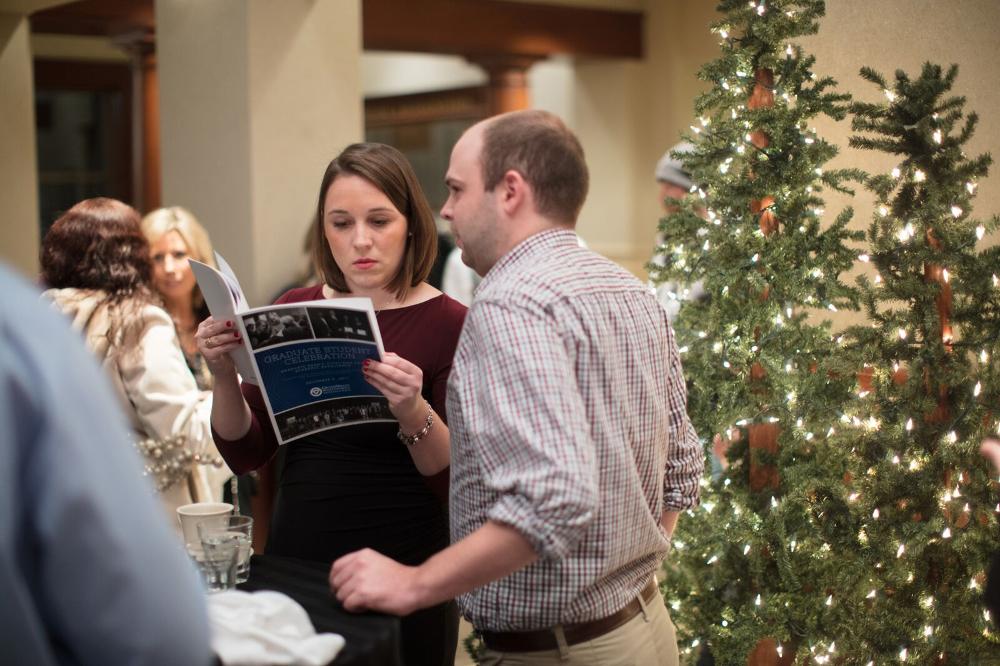 People standing near decorative christmas trees, looking through a program together